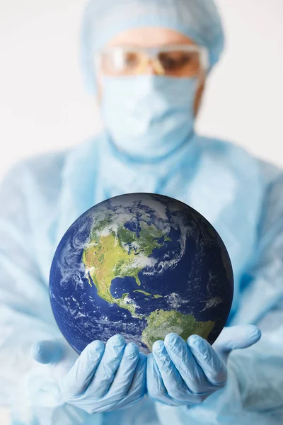Close up of doctor hand holding earth. Mock up. Medical equipment. A doctor wearing personal protective equipment including mask, goggle, and suit to protect COVID 19 coronavirus infection.