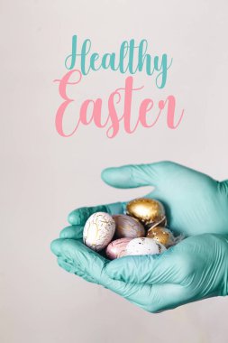 Modern boyalı paskalya yumurtalarını tutan tıbbi eldivenli eller. Seçici odaklanma. Tonlu resim. İzole edilmiş. Sağlıklı Paskalya metni.