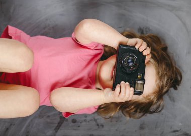 Kameralı küçük kız fotoğrafçı gülümsüyor ve fotoğraf çekiyor. Üst görünüm.