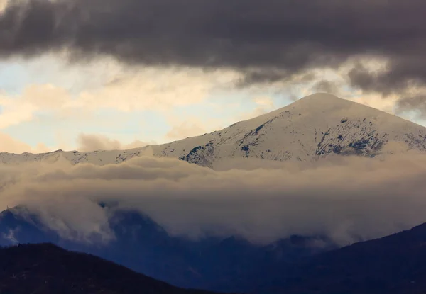 Une montagne enneigée entourée de nuages blancs et sombres — Photo