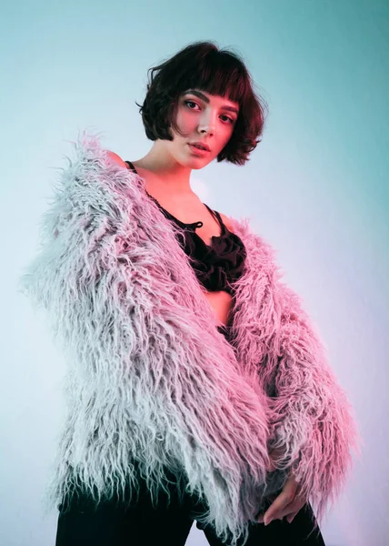 Young girl in a pink fur coat blue background studio red light