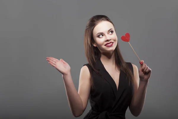 Girl holding paper heart, isolated, gray background. Joyful young fashion woman smiling. showing empty copy space on open hand palm — Stock Photo, Image