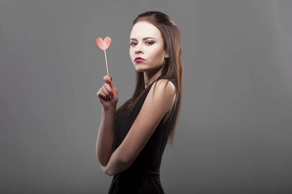 Girl holding red paper heart, isolated, gray background. young fashion with serious face emotion woman. — Stock Photo, Image
