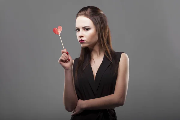 Girl holding red paper heart, isolated, gray background. young fashion with serious face emotion woman. — Stock Photo, Image