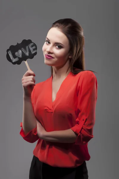 Mujer morena sensual de moda bastante sexy posando sobre fondo gris vestida con camisa roja, sosteniendo palos de fiesta de papel. Amor. —  Fotos de Stock