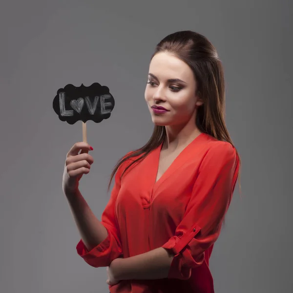 Mujer morena sensual de moda bastante sexy posando sobre fondo gris vestida con camisa roja, sosteniendo palos de fiesta de papel. Amor. —  Fotos de Stock