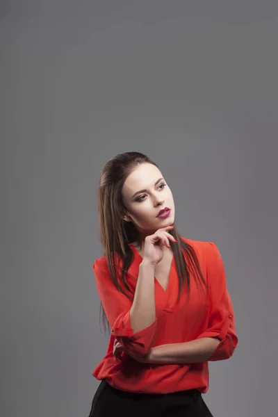 Ragazza in camicia rossa, sfondo grigio. Gioioso giovane donna bruna di moda. Pensare — Foto Stock