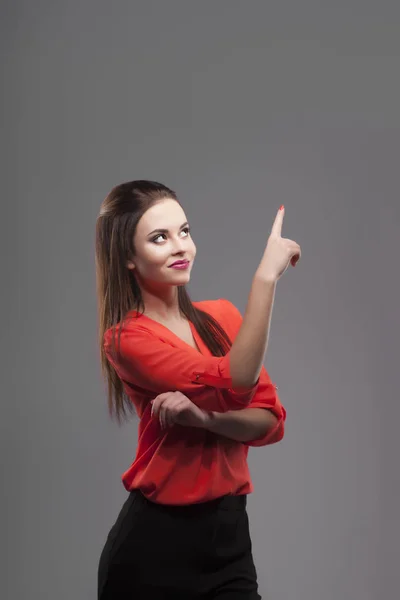Ragazza in camicia rossa, sfondo grigio. Giovane donna allegra e sorridente. mostrando lo spazio di copia vuoto a mano delle dita — Foto Stock