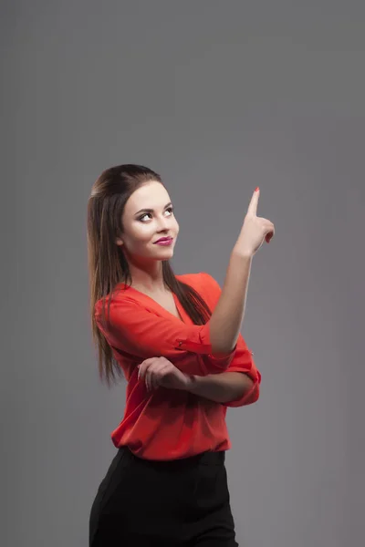 Fille en chemise rouge, fond gris. Joyeuse jeune femme de mode souriante. montrant l'espace de copie vide par la main du doigt — Photo