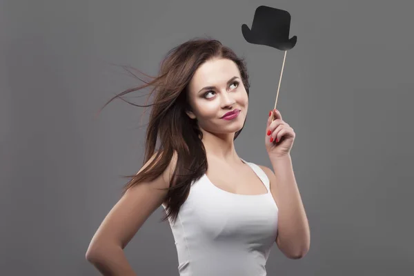 Menina segurando chapéu de cilindro de papel engraçado na vara, isolado, fundo cinza. Joyful jovem mulher da moda sorriso, movimento do cabelo — Fotografia de Stock
