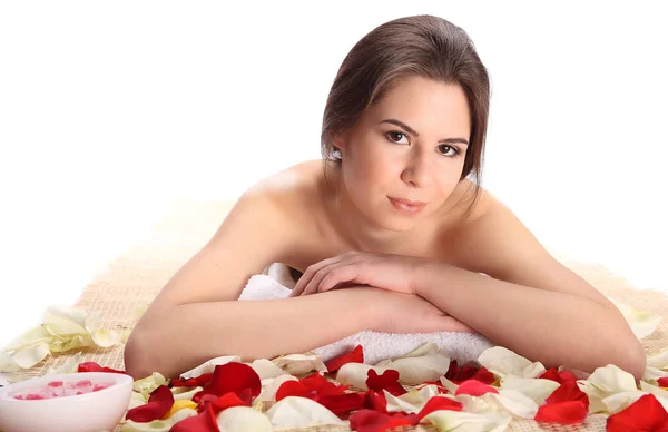 Primer plano Mujer hermosa, joven y saludable en el salón de spa en la estera de bambú con pétalos de rosa. Spa, concepto de salud y curación . — Foto de Stock