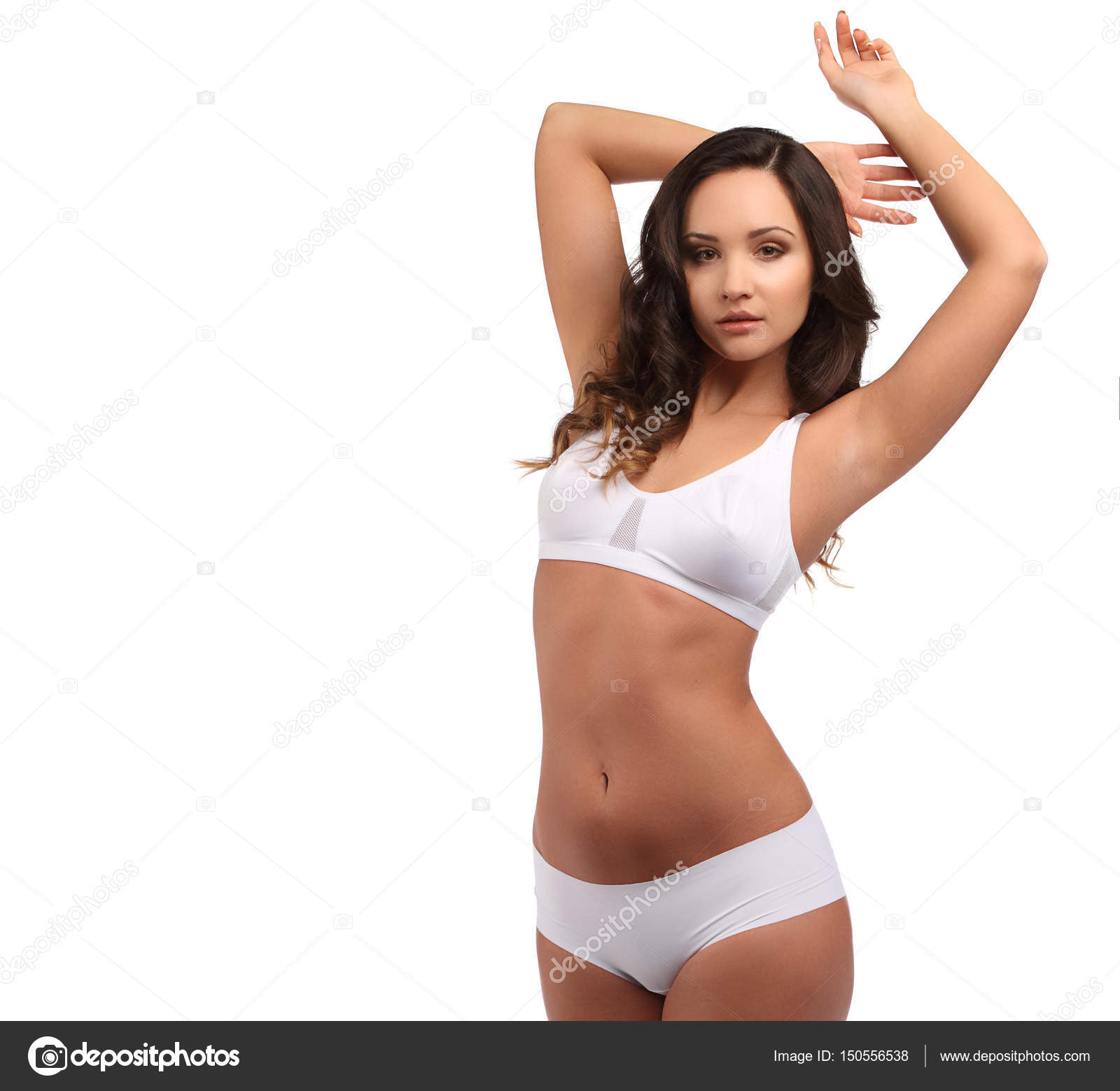 Young brunette woman with tanned skin and curly hair in white cotton panties  and sports bra isolated on white, hands up Stock Photo by ©fenixlive  150556538