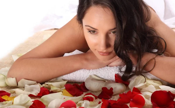 Mulher relaxada feliz bonita no spa do dia da saúde com tratamento de massagem que coloca na toalha branca na mesa de bambu decorada com pétalas de rosa — Fotografia de Stock