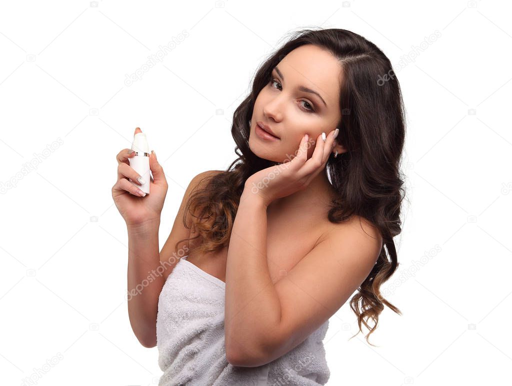 Young curly brunette woman in bath towel holding lotion for her skin, moisturizing
