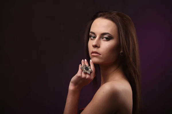 Όμορφη μελαχρινή γυναίκα με επαγγελματικό μακιγιάζ και χτένισμα δείχνει μεγάλο δαχτυλίδι και σκουλαρίκια. διαφήμιση κοσμήματα — Φωτογραφία Αρχείου