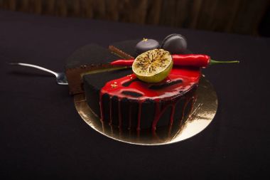 Kek ile siyah kadife kaplı. kireç, biber ve macaroons, üstte kırmızı sır. Siyah arka plan üzerine kesilmiş bir parça ile modern bir pasta