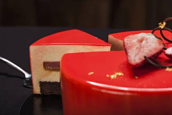 Полуничний торт, покритий червоною дзеркальною глазур'ю, прикрашеною шматочками ягід, золотом та шоколадом. Сучасний торт з вирізаним шматком крупним планом — стокове фото