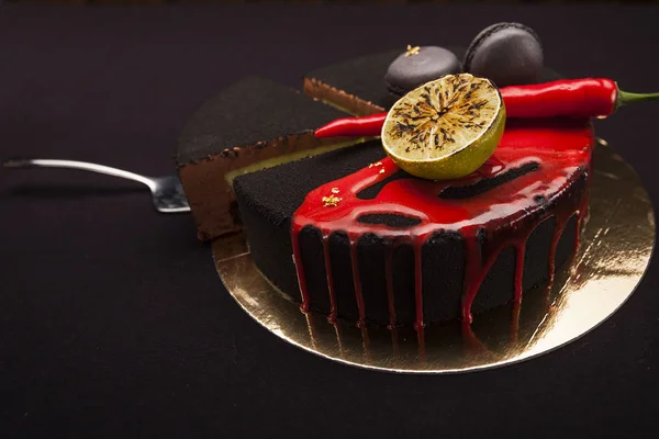 Kuchen mit schwarzem Samt bedeckt. Limette, Chilischote und Makronen, darüber rote Glasur. geschnittenes Stück auf goldenem Teller — Stockfoto