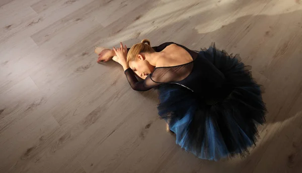 Bovenaanzicht van de professionele ballerina in blauwe tutu en pointe schoenen zitten en stretching op verdieping. Copyspace — Stockfoto