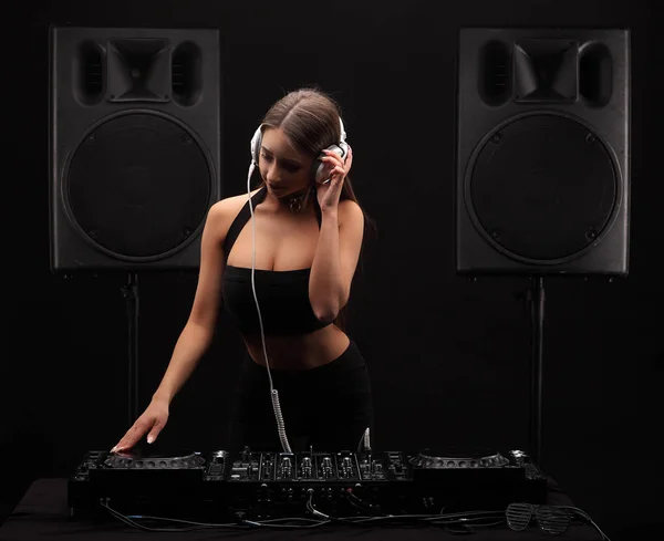 Young sexy brutette woman dj with long hair in white headphones playing music on mixer on table. Loudspeakers on background — Stock Photo, Image