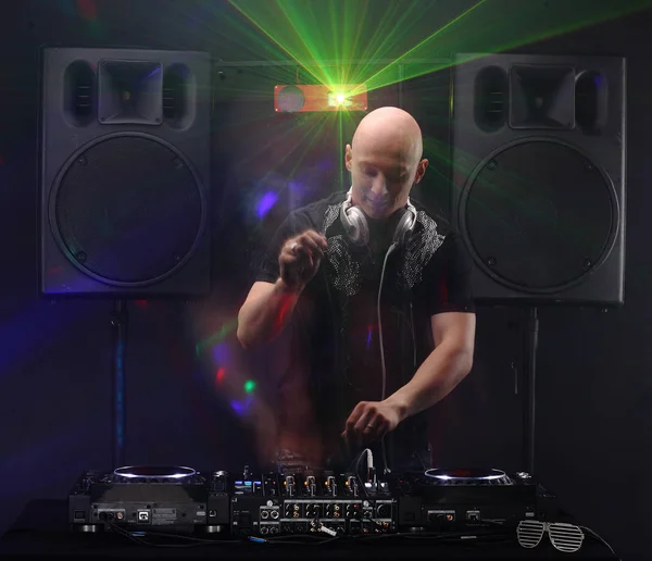 Club DJ with white headphones playing mixing music on turntable and dancing at party. Loudspeakers and lasers on background. slow sync flash technique