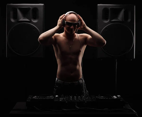 Bold adulto DJ fica perto misturador entre dois grandes alto-falantes seminua com fones de ouvido brancos e mãos na cabeça — Fotografia de Stock