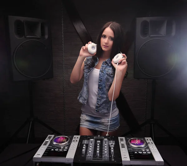 Dj woman showing white headphones playing music on mixer with light beam effects. Loudspeakers on background. — Stock Photo, Image