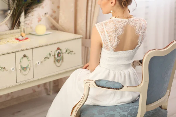 Esküvő előkészítés. Gyönyörű fiatal menyasszony fehér esküvői ruha bent. Luxus modell vintage szék otthoni stúdióban ül — Stock Fotó