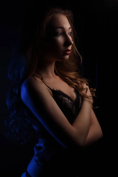 Sexy giovane bella donna con riccioli in lingerie nera sensuale, illuminata con blu in studio ritratto — Foto Stock