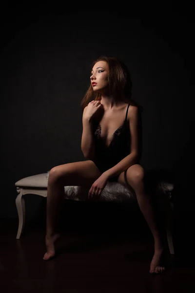 Sexy brünette Frau in sinnlichen schwarzen Dessous, sitzt auf einer weißen Bank mit Fell, barfuß. — Stockfoto