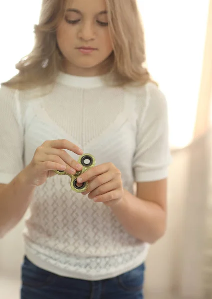 Cute młoda dziewczyna w białej koszuli, grając z fidget zielony spinner w jasny pokój — Zdjęcie stockowe