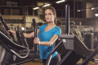 Genç bir eliptik eğitmen fitness merkezinde kullanan kadın geri vurdu yerleştirmek. Spor salonunda fitness kız portresi.