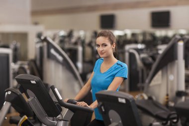 Genç kadın fitness merkezinde kalbî bir bisiklet kullanarak yerleştirmek. Fitness salonunda, yaşam kavramı kız portresi.