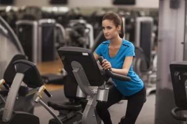 Genç kadın fitness merkezinde kalbî bir bisiklet kullanarak yerleştirmek. Fitness salonunda, yaşam kavramı kız portresi.