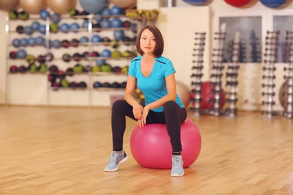 Kadın oturup pembe bir Pilates topu kapalı spor salonu arka plan.