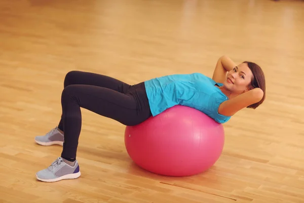 Donna che esercita i suoi addominali su una palla rosa Pilates al chiuso . — Foto Stock