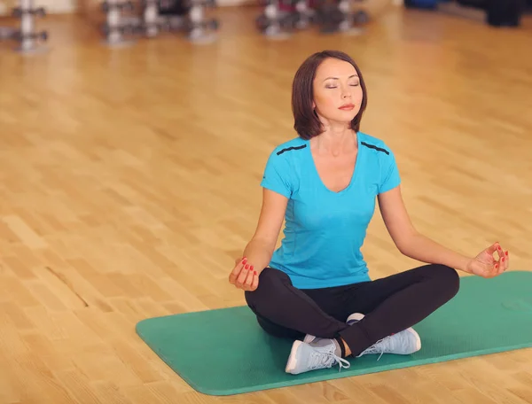 Femme aérobic sport gymnase exercices sur le sol, fille s'asseoir sur le tapis dans la pose de yoga . — Photo