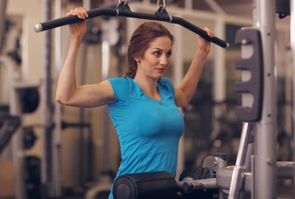 Strong woman in blue t-shirt and black pants exercising in a gym - doing pull-ups.