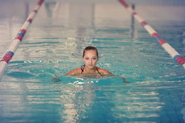 Nuotatrice in una piscina sportiva coperta. ragazza in tuta rosa in acqua — Foto Stock