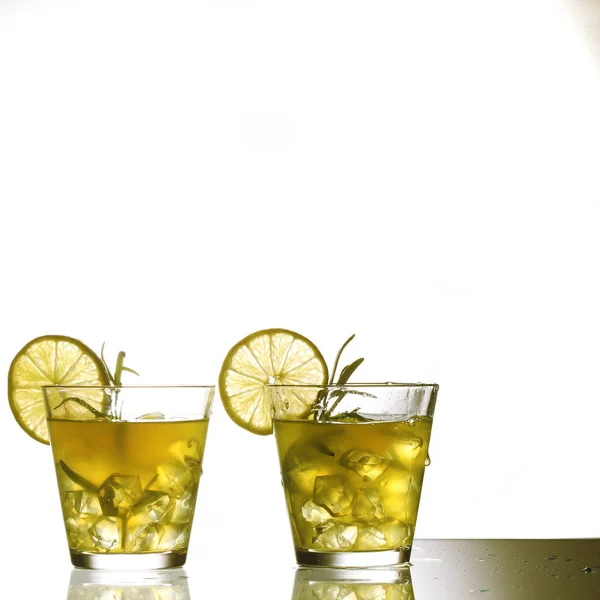 Dois coquetéis amarelos com limão e alecrim em pé sobre vidro em estúdio, isolados — Fotografia de Stock