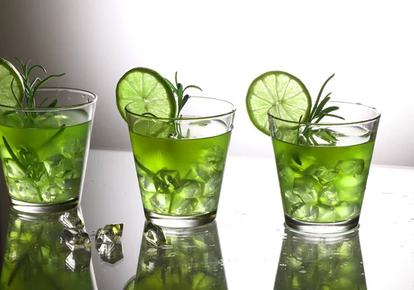 Три зелених коктейлі з лаймом і розмарином, що стоять на склі в студії, сірий фон — стокове фото