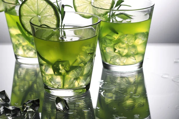 Tre cocktail verdi con lime e rosmarino in piedi su vetro in studio, sfondo grigio — Foto Stock