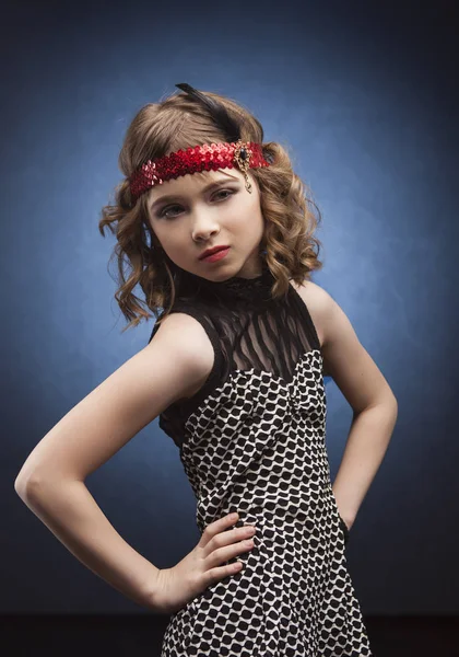 Beautiful little fashion model walking on catwalk in studio on background lighted with blue. Aggressove look, red lips and dressed in the style of a 20\'s Great Gatsby on party