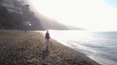 Sabah güneş doğarken Sahilde yürüyüş güzel sarışın genç kadın. Amalfi coast, İtalya.