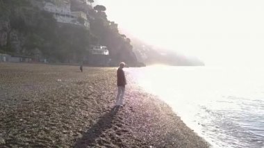 Sabah güneş doğarken Sahilde yürüyüş güzel sarışın genç kadın. Amalfi coast, İtalya.