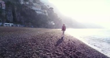 Sabah güneş doğarken Sahilde yürüyüş güzel sarışın genç kadın. Amalfi coast, İtalya.