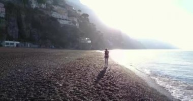 Sabah güneş doğarken Sahilde yürüyüş güzel sarışın genç kadın. Amalfi coast, İtalya.