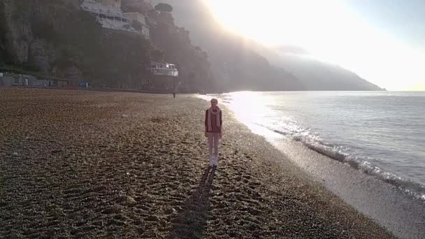 Szép fiatal szőke nő séta a tengerparton a reggel napkeltekor. Amalfi coast, Olaszország. — Stock videók