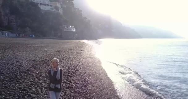 美丽年轻的金发女郎海滩上散步，在早晨的日出。阿马尔菲海岸意大利. — 图库视频影像