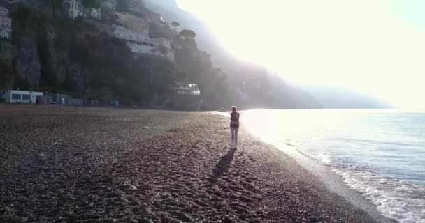 Krásná mladá blondýnka procházky na pláži na ranní východ slunce. Amalfské pobřeží, Itálie. — Stock video